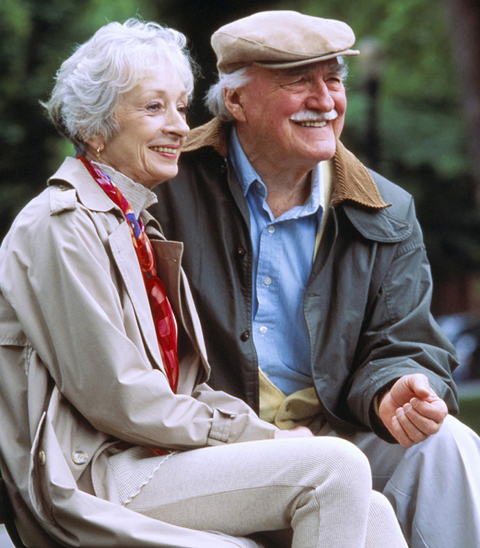 A senior couple on a park bench looking at the park smiling.